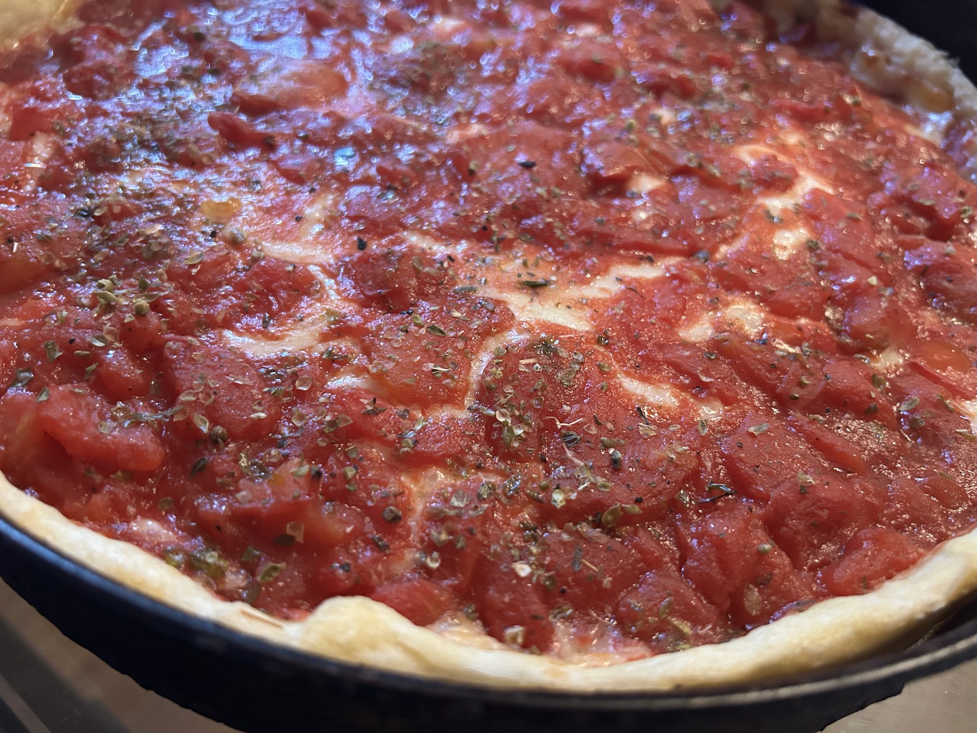 Close-up of a deep dish pizza with chunky tomato sauce and dried herbs in a black pan